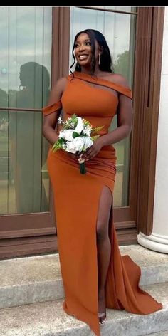 a woman in an orange dress standing on steps with her legs crossed and holding a bouquet