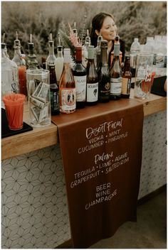 a woman standing behind a counter filled with liquor bottles and glasses on top of it