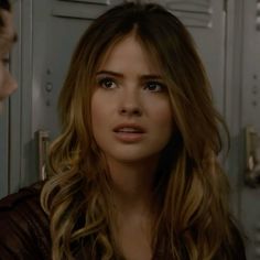 a woman standing in front of a locker with another person behind her looking at her