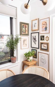 a dining room table with chairs and pictures on the wall above it, next to a potted plant