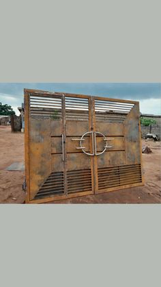 an old rusted metal gate in the middle of a dirt field with a cross on it