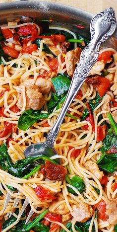 a pan filled with pasta and spinach on top of a wooden table next to a fork