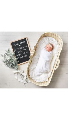 a baby is laying in a basket next to a chalkboard with the birth date on it