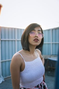 a woman wearing pink sunglasses standing in front of a blue fence and looking off into the distance