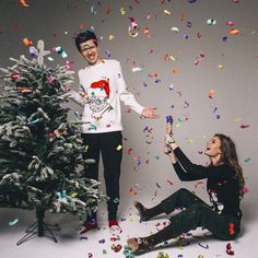 two people sitting in front of a christmas tree with confetti on the ground