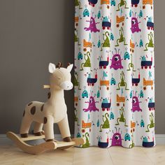 a wooden rocking horse next to a curtain with colorful cartoon animals on it's side