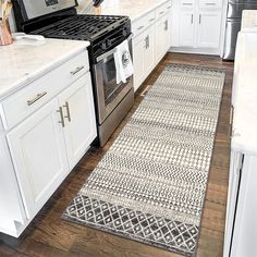 a kitchen with white cabinets and an area rug on the floor in front of the stove