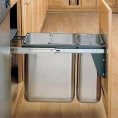 two stainless steel trash cans are in the middle of a kitchen cabinet with wooden floors