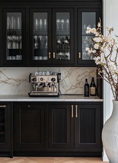 a kitchen with black cabinets and white marble counter tops, wine glasses on the cabinet doors