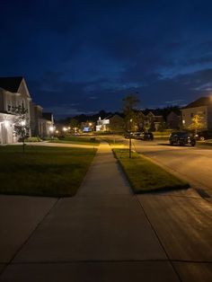 an empty street at night with cars parked on the side and houses in the background