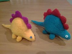 two knitted dinosaurs sitting on top of a wooden table