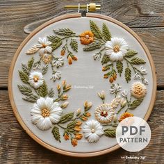 an embroidery pattern with white and orange flowers on a wooden surface, in the shape of a circle