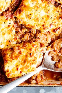 a pan filled with meat and rice covered in sauce next to a serving utensil