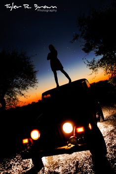 a person standing on the hood of a jeep at night with trees in the background