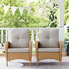 two wicker chairs sitting on top of a porch next to each other in front of a tree