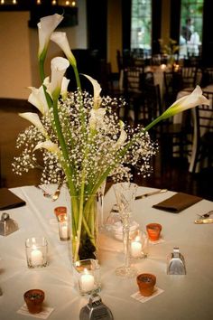 a vase filled with white flowers sitting on top of a table next to lit candles