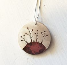 a necklace with an image of trees and berries on the front, hanging from a silver chain