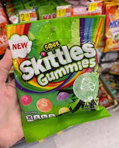 a hand holding a bag of skittles gummies