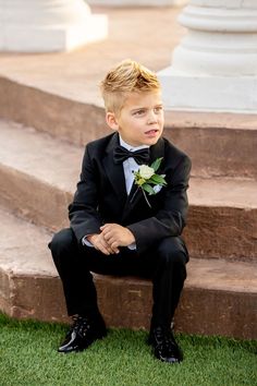 a young boy in a tuxedo sitting on some steps wearing a boutonniere