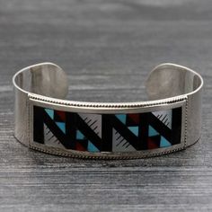 Zuni bracelet featuring traditional inlay of turquoise, coral, shell and jet handcrafted by artist Leander & Lisa Othole (Hallmark etched script Leander & Lisa Othole, Zuni). Bracelet is 3/4" wide, 5 1/2" tip to tip inside with an 1' opening which will fit a wrist circumference of up to 6 1/2". Bracelet weighs 26 grams. Artisan Sterling Silver Bracelet With Inlay, Traditional Inlay Cuff Bangle Bracelet, Traditional Adjustable Cuff Bracelet With Inlay, Traditional Adjustable Inlay Bracelets, Traditional Adjustable Inlay Cuff Bracelet, Traditional Black Engraved Bracelets, Artisan Black Bangle Jewelry, Traditional Inlay Bracelets Perfect For Gifts, Traditional Inlay Bracelets As Gift