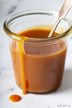 a glass jar filled with caramel sauce on top of a white counter next to a spoon