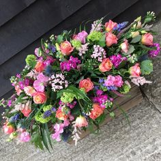 a wooden box filled with lots of colorful flowers on top of a cement floor next to a wall