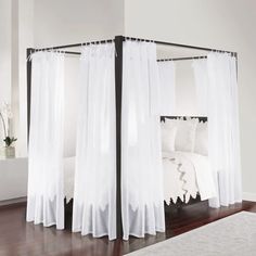 a canopy bed with sheer curtains over it in a white and black bedroom, along with hardwood flooring