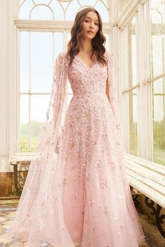 a woman standing in front of a window wearing a pink gown