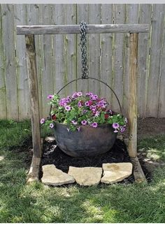 a potted plant sitting on top of a wooden stand next to a fence with flowers in it