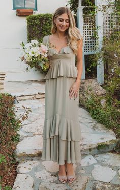 a woman in a long dress holding a bouquet and standing on the steps outside her house