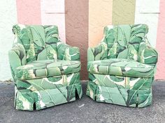 two green chairs sitting next to each other in front of a wall with palm leaves on it