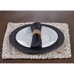 a place mat with a black napkin on top of it and a white plate in the middle