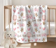 a teddy bear sitting next to a baby crib with hearts and hot air balloons