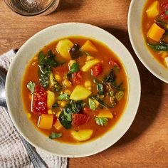 two bowls of vegetable soup on top of a wooden table next to a glass of water