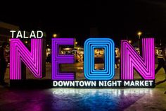 neon sign that says neon downtown night market in front of people walking by at night