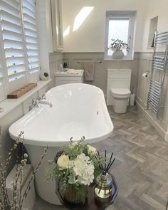 a large white bath tub sitting next to a toilet in a bathroom on top of a hard wood floor