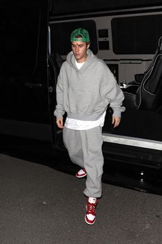 a man in grey hoodie and red sneakers stepping out of a van