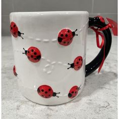 a coffee mug with ladybugs painted on it and a red ribbon around the handle