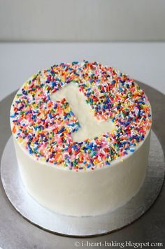 a white cake with sprinkles and a letter t on the top is sitting on a silver platter