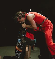 a man in red jumpsuit standing on one leg while another person holds his head down