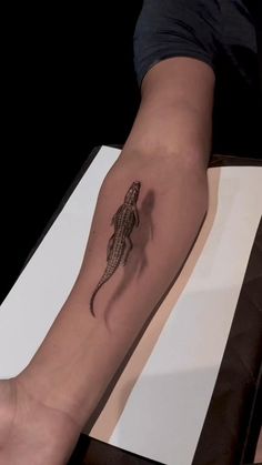 a person's arm with a small lizard tattoo on the left side of their arm