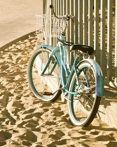 a blue bike parked next to a fence on the side of a beach with sand