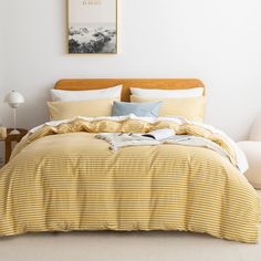 a bed with yellow and white striped comforter next to a painting on the wall