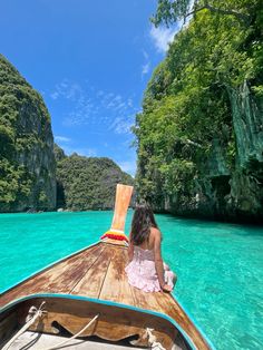 a woman sitting on the bow of a boat in clear blue water, surrounded by trees