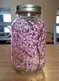 a glass jar with pink flowers painted on it sitting on top of a wooden table