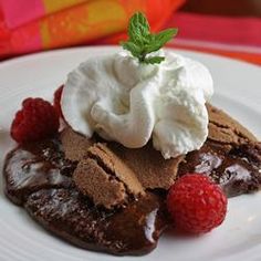 a chocolate dessert with whipped cream and raspberries on a plate next to a gift bag