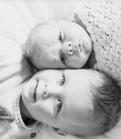 two young children laying on top of each other in black and white photo with the baby looking at the camera