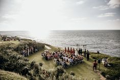 a group of people standing on top of a lush green field next to the ocean