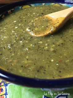 a wooden spoon in a blue bowl filled with green liquid and spices, on top of a colorful table cloth