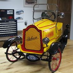 an old fashioned yellow car on display in a room with wood flooring and tools